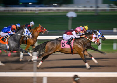 Horse race with jockeys sprinting on the track at night.
