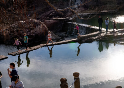People walking on a narrow stone path over a calm river with reflections.